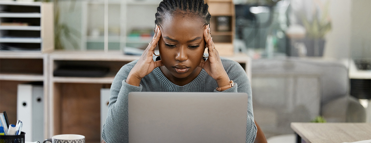 Frustrated woman sitting in front of laptop with her hands on her temples.