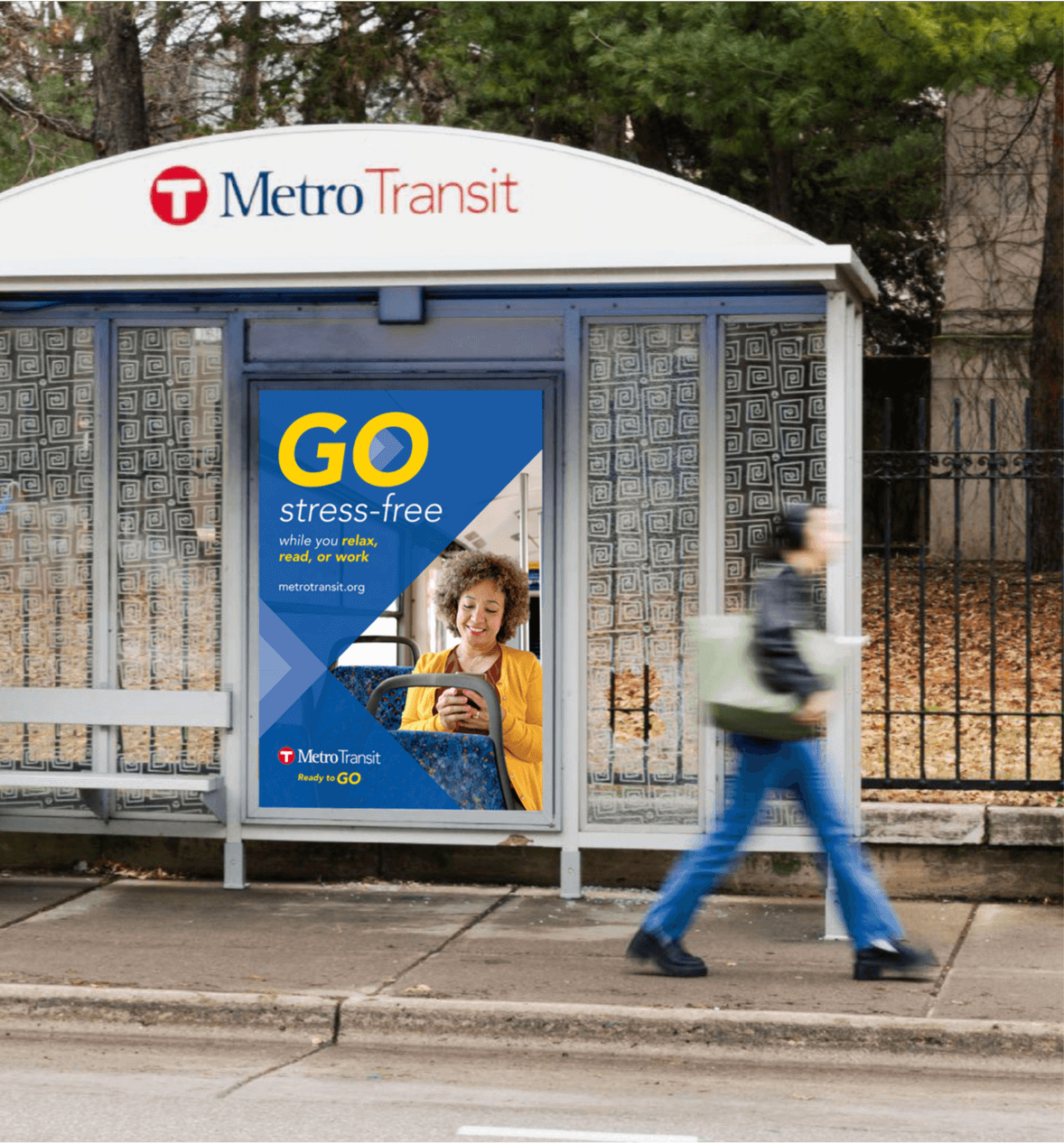 A bus shelter featuring an ad that says, "GO stress-free while you relax, read or work," with an image of an older woman using her phone while sitting on the bus.