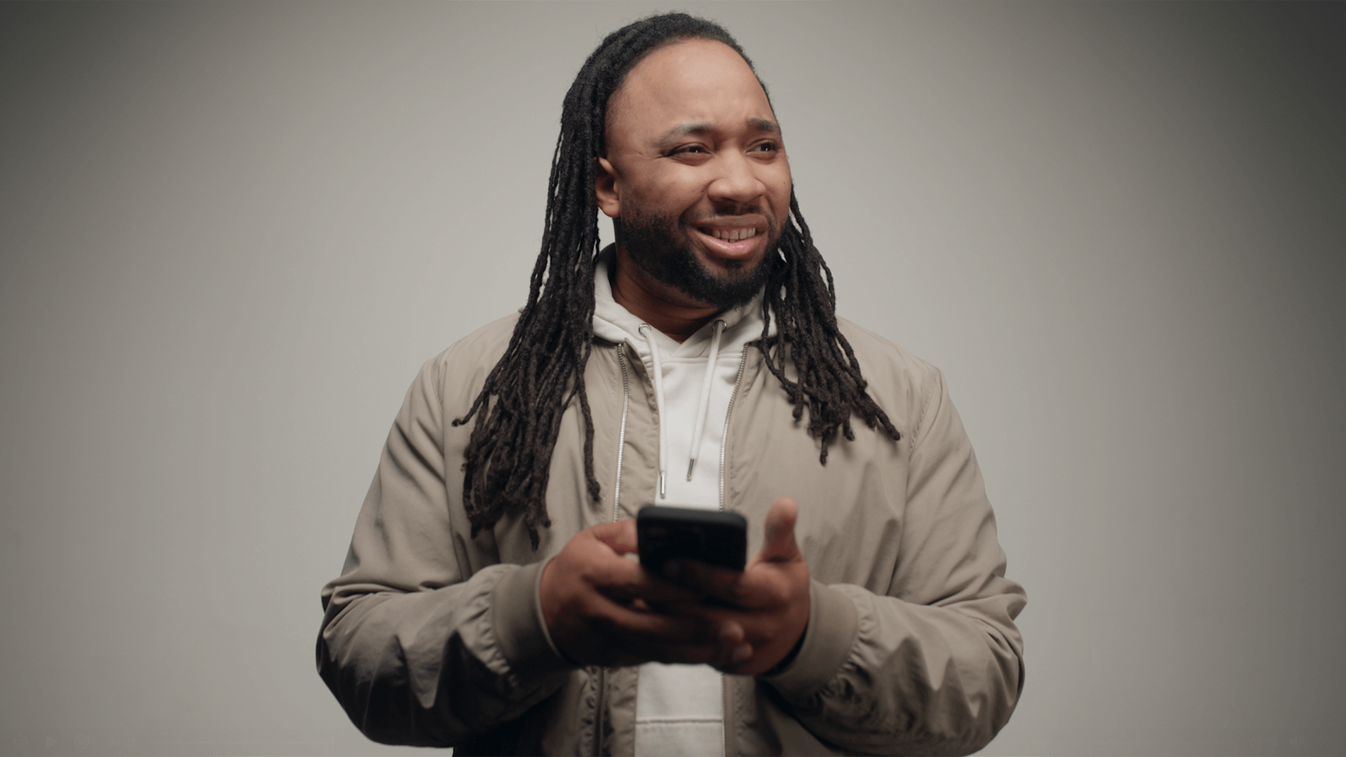 Man with dreadlocks looking confused and holding a phone.