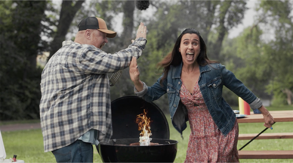 CCF_QuitPartner_VideoThumbnail2 A man and woman stand outside next to a charcoal grill. They are overacting as they high five after throwing a pack of cigarettes onto the grill.